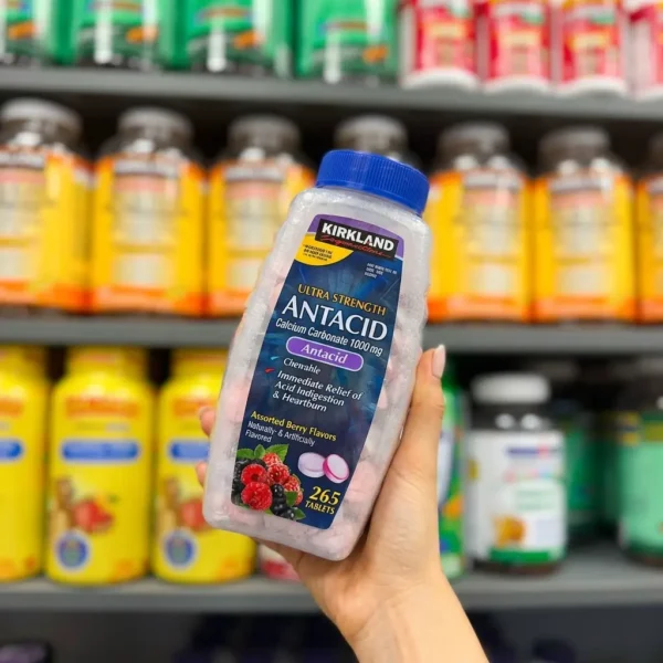 بطری آنتی اسید کرکلند Ultra Strength در دست با پس‌زمینه قفسه مکمل‌ها